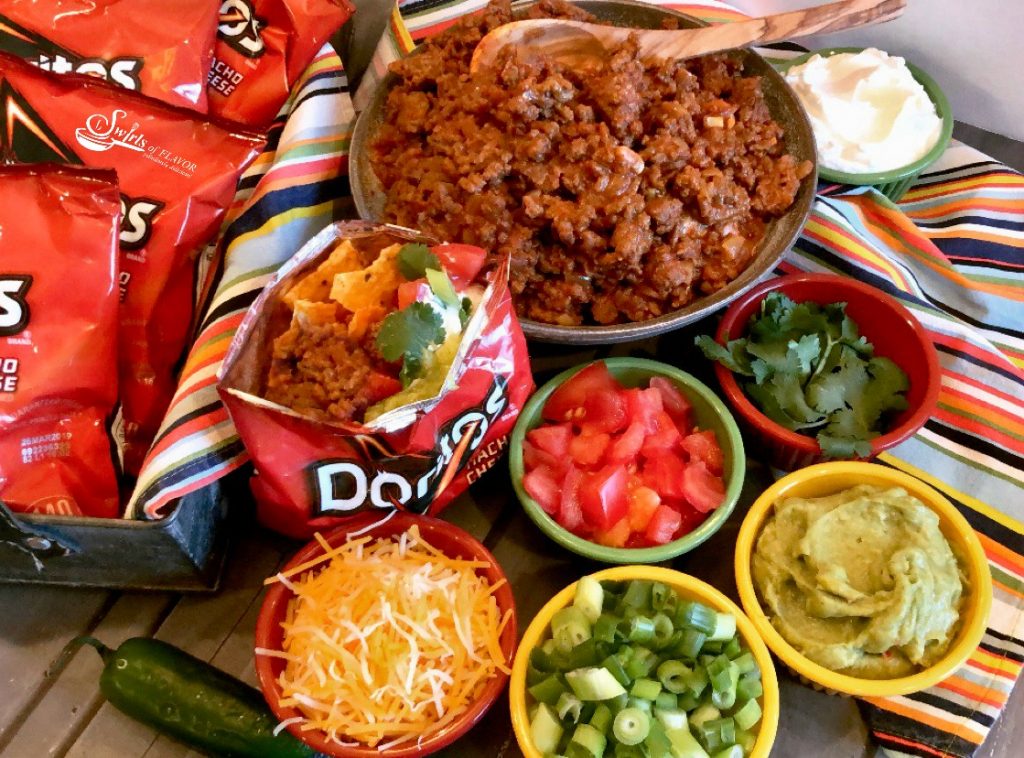 Our Walking Taco Bar is the perfect way to serve up a saucy taco filling and your favorite toppings for the big game. Crush the chips in your bag, top them with a flavorful beef taco filling, pile high with lots of taco toppings, add a plastic fork and you’re all set! #beeftaco #portabletaco #walkingtacobar #tacosinabag #funforkids #gamedayfood #superbowl #easyrecipe #entertaining #swirlsofflavor